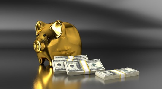 Image of a gold piggy bank with stacks of money laid aside it.